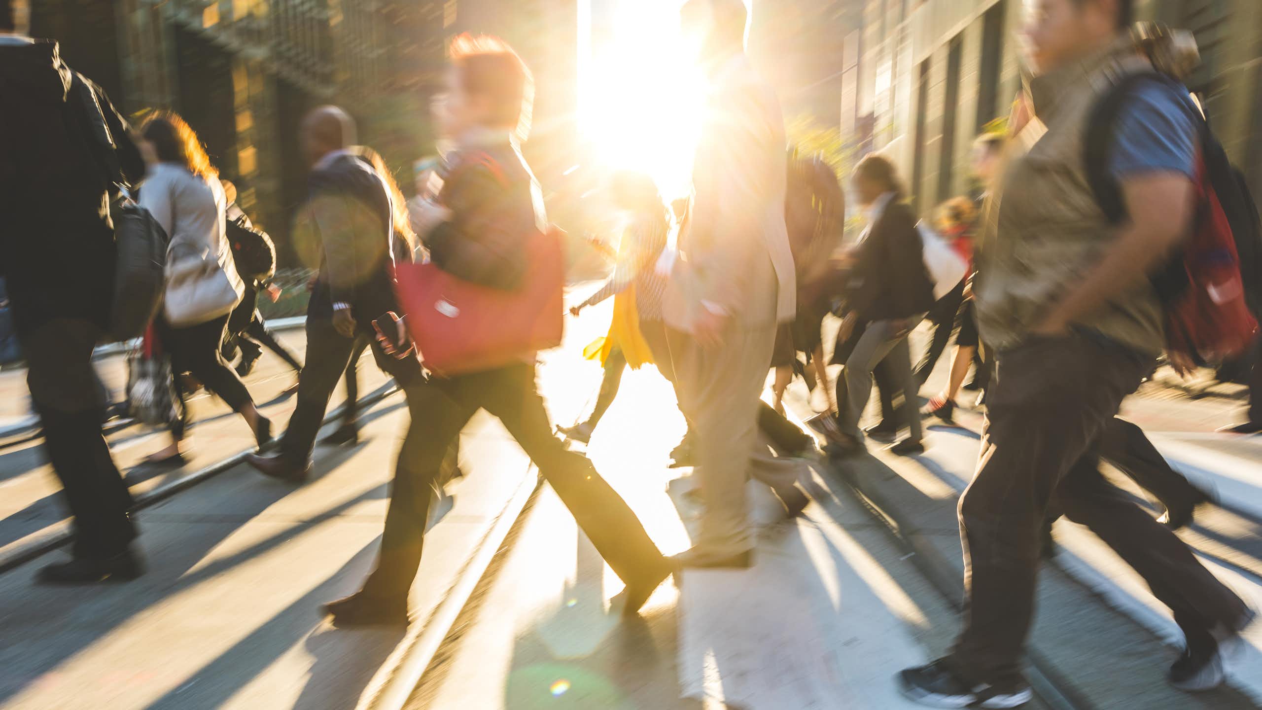 blurred shot of commuters crossing a street as the sun sets.