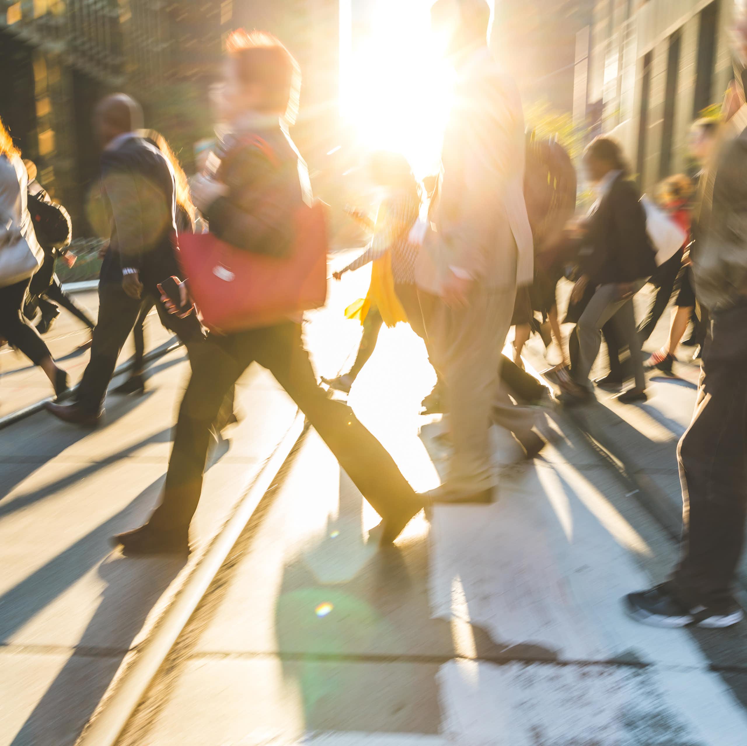 blurred shot of commuters crossing a street as the sun sets.