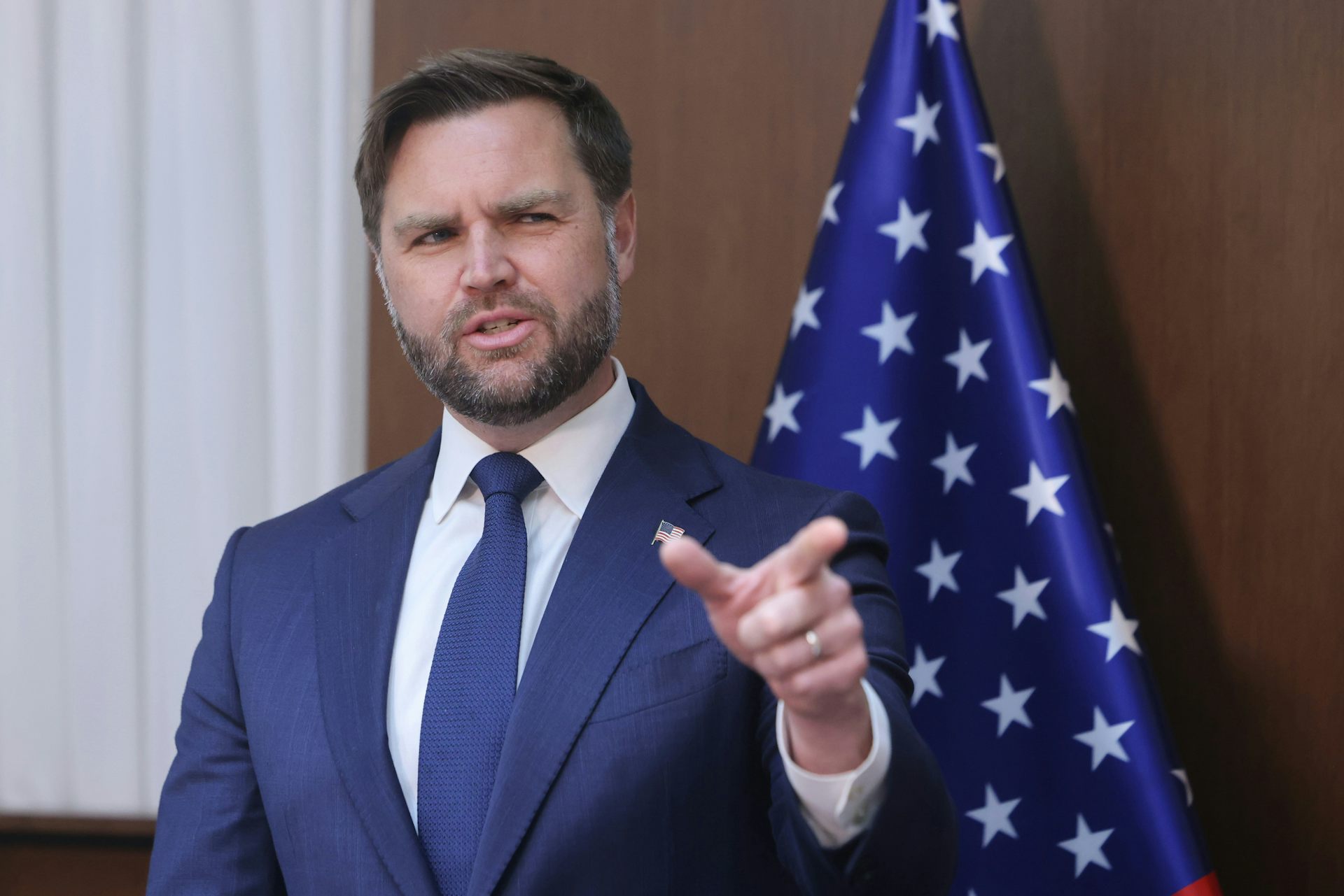 US vice-president, J.D. Vance points towards the camera while standing in front of a stars and stripes flag.