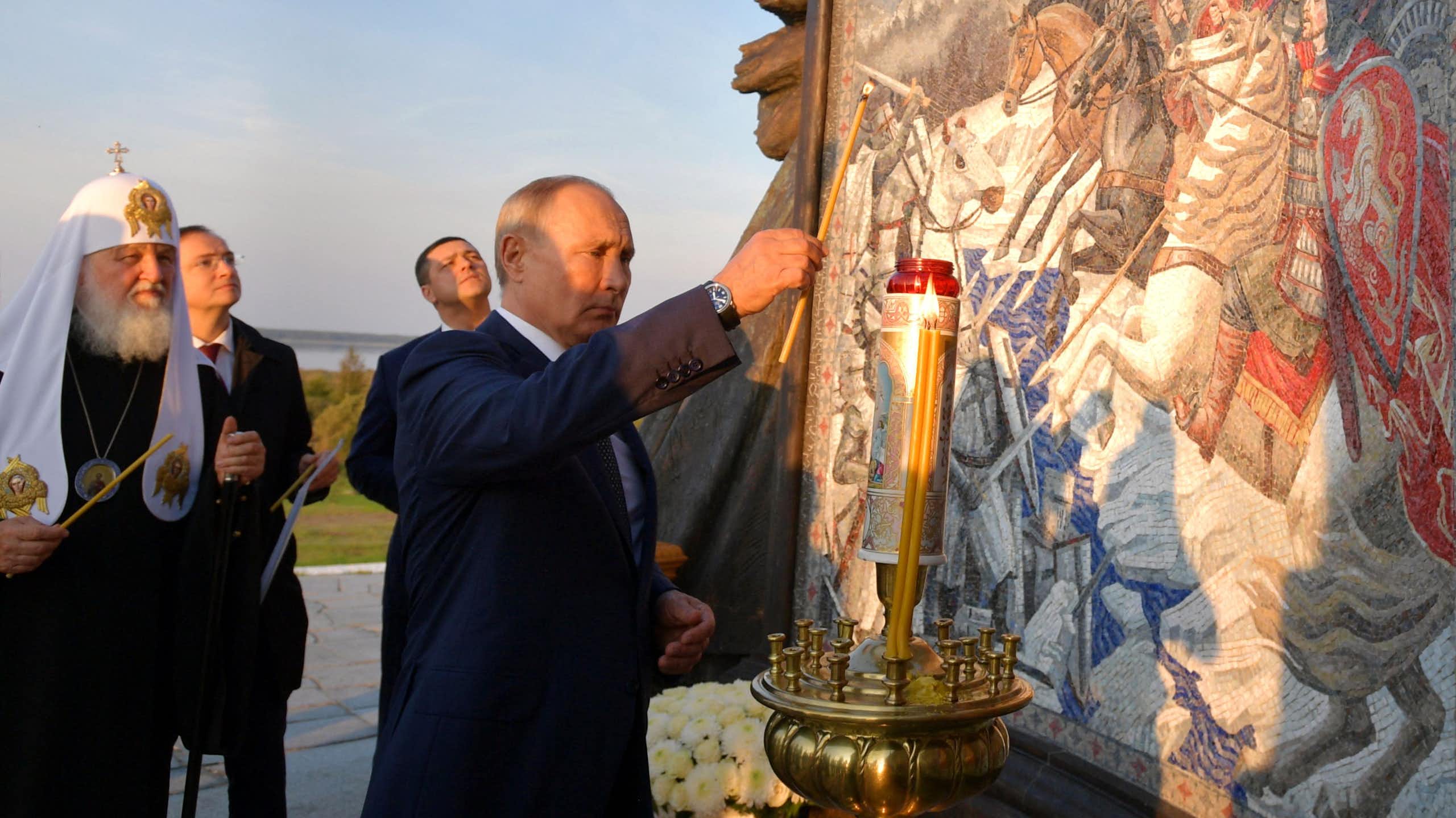 A man lights a candle next to a statue and engraving.
