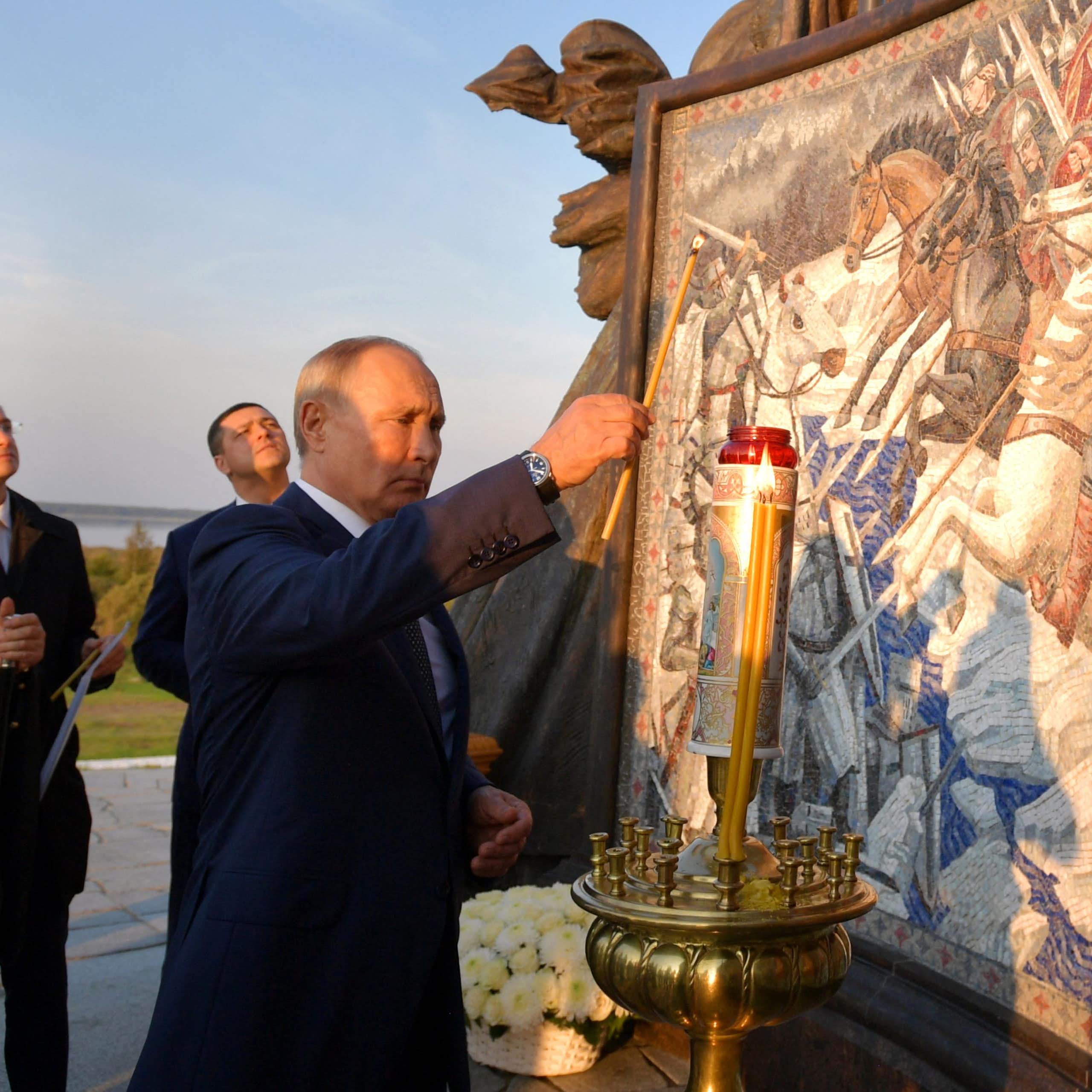 A man lights a candle next to a statue and engraving.