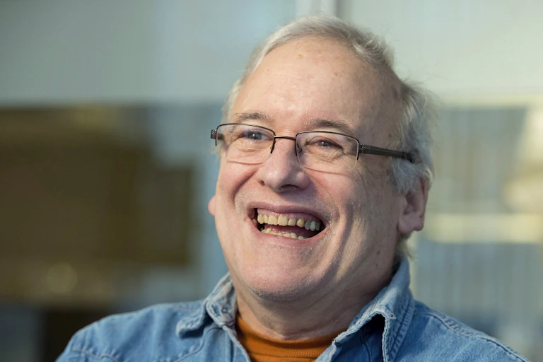 A man with a wide smile and glasses laughs.