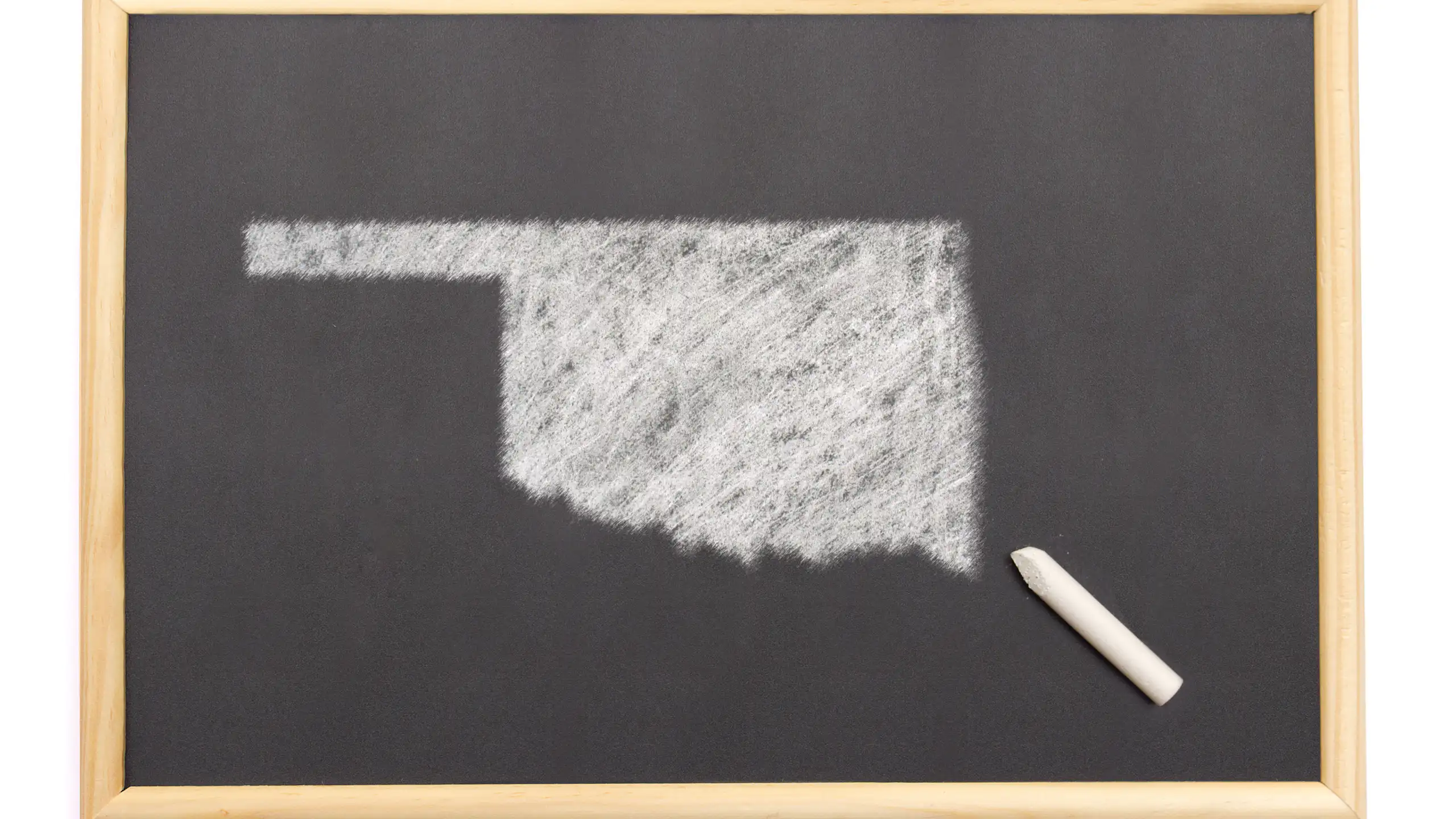 A top shot of an isolated blackboard with a chalk and the shape of Oklahoma drawn onto it.