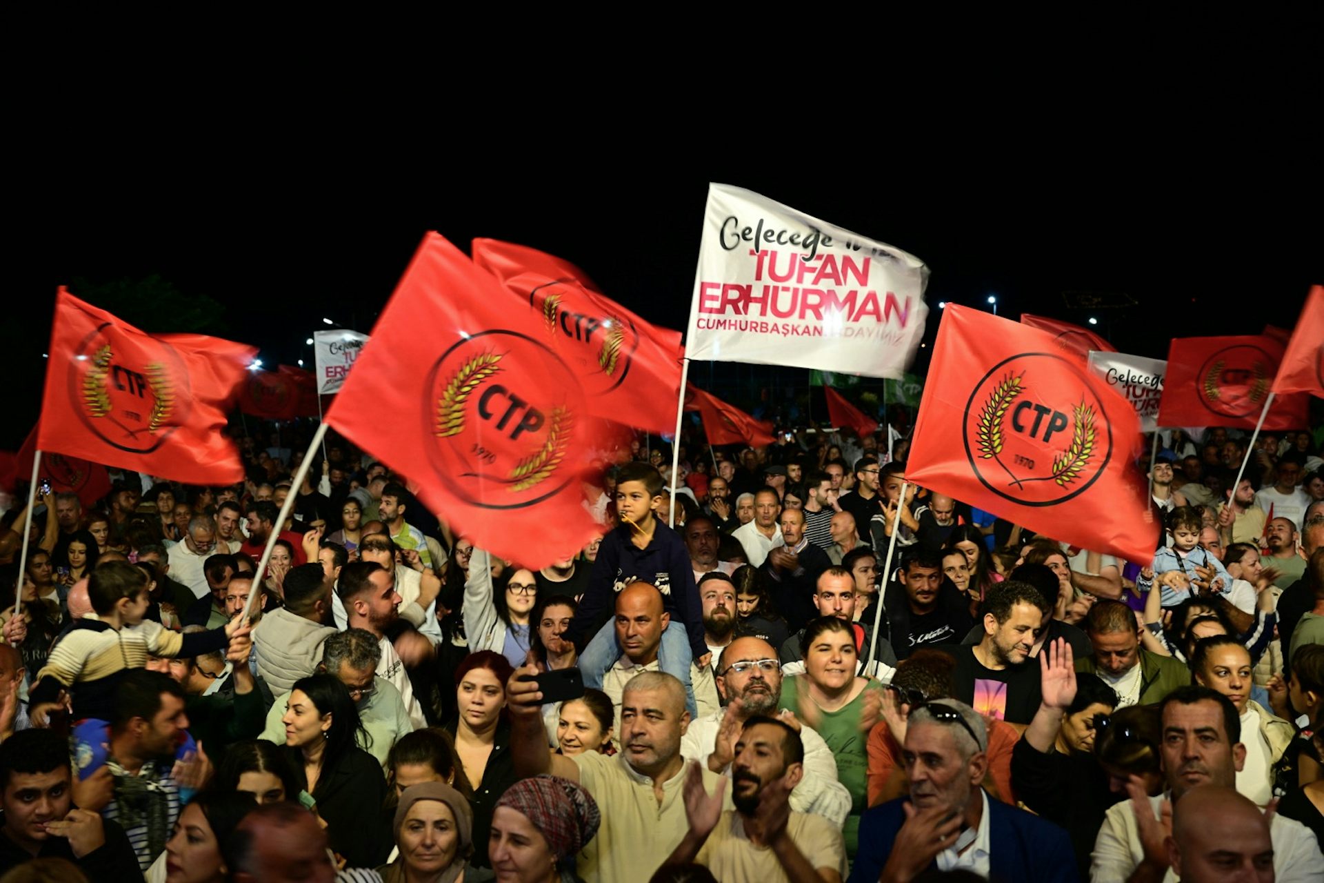 A crowd of smiling people wave red flags and banners.