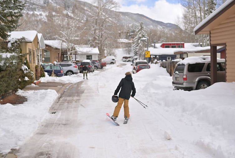 A teenager on skis traverses a snowy mobile home park.