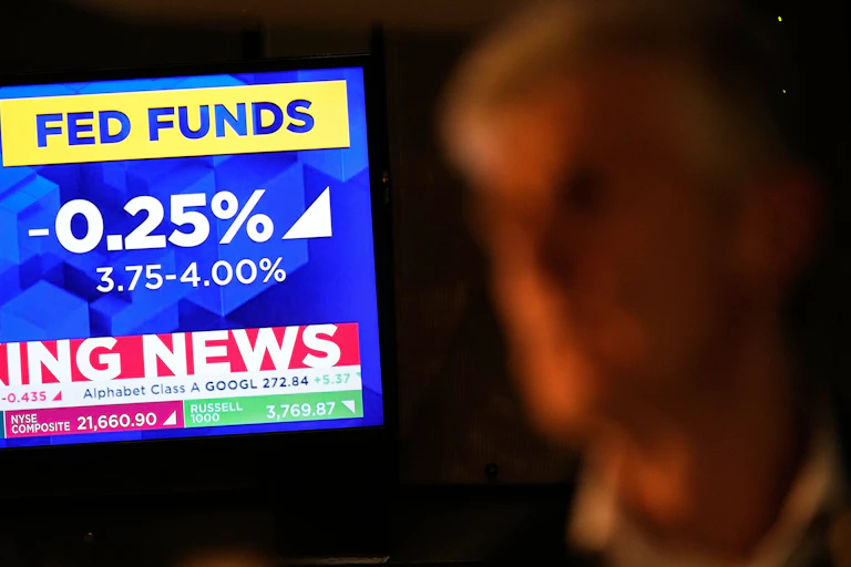 A tv screen displays news about the fed rate cut as a trader looks on
