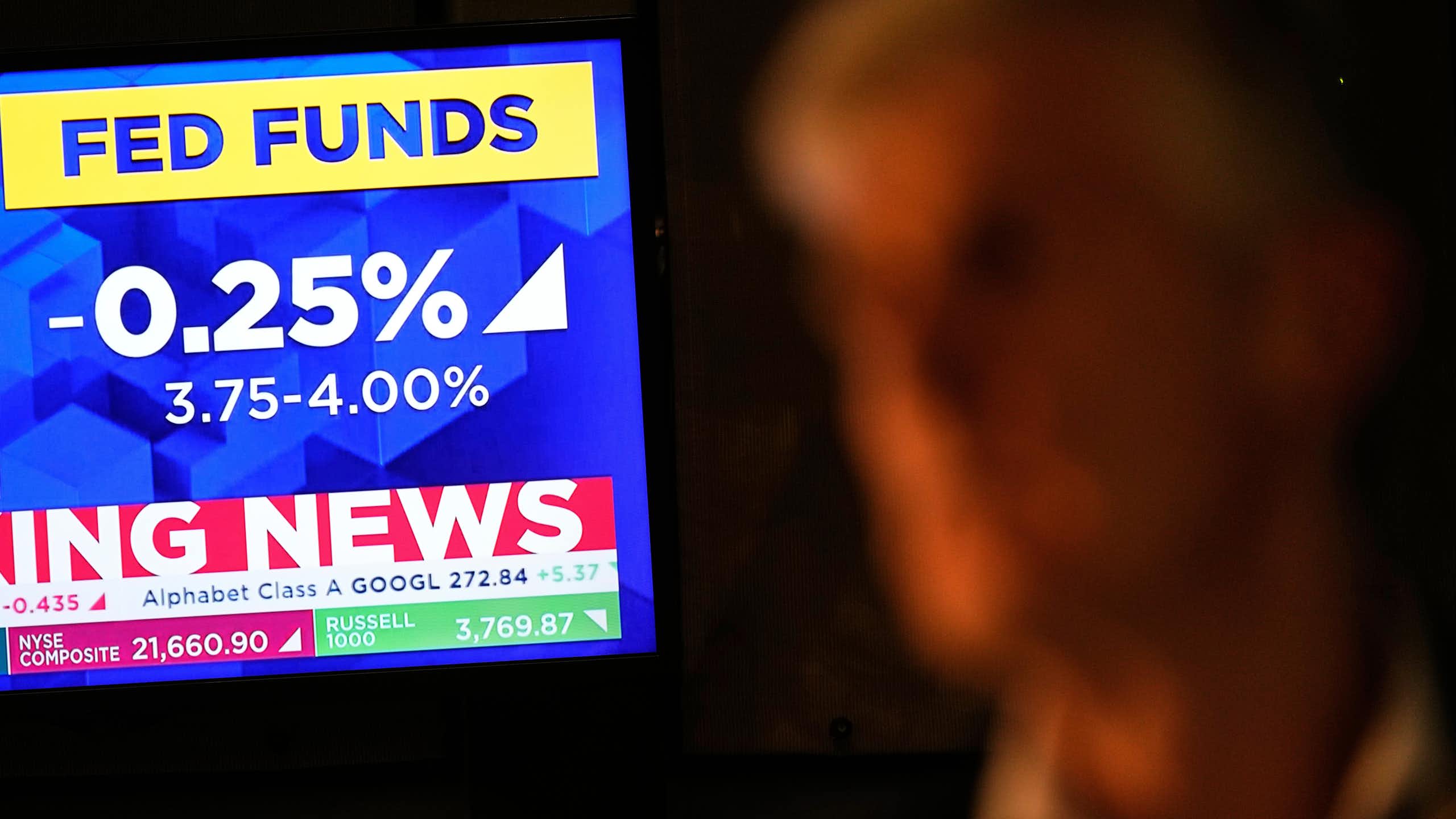 A tv screen displays news about the fed rate cut as a trader looks on