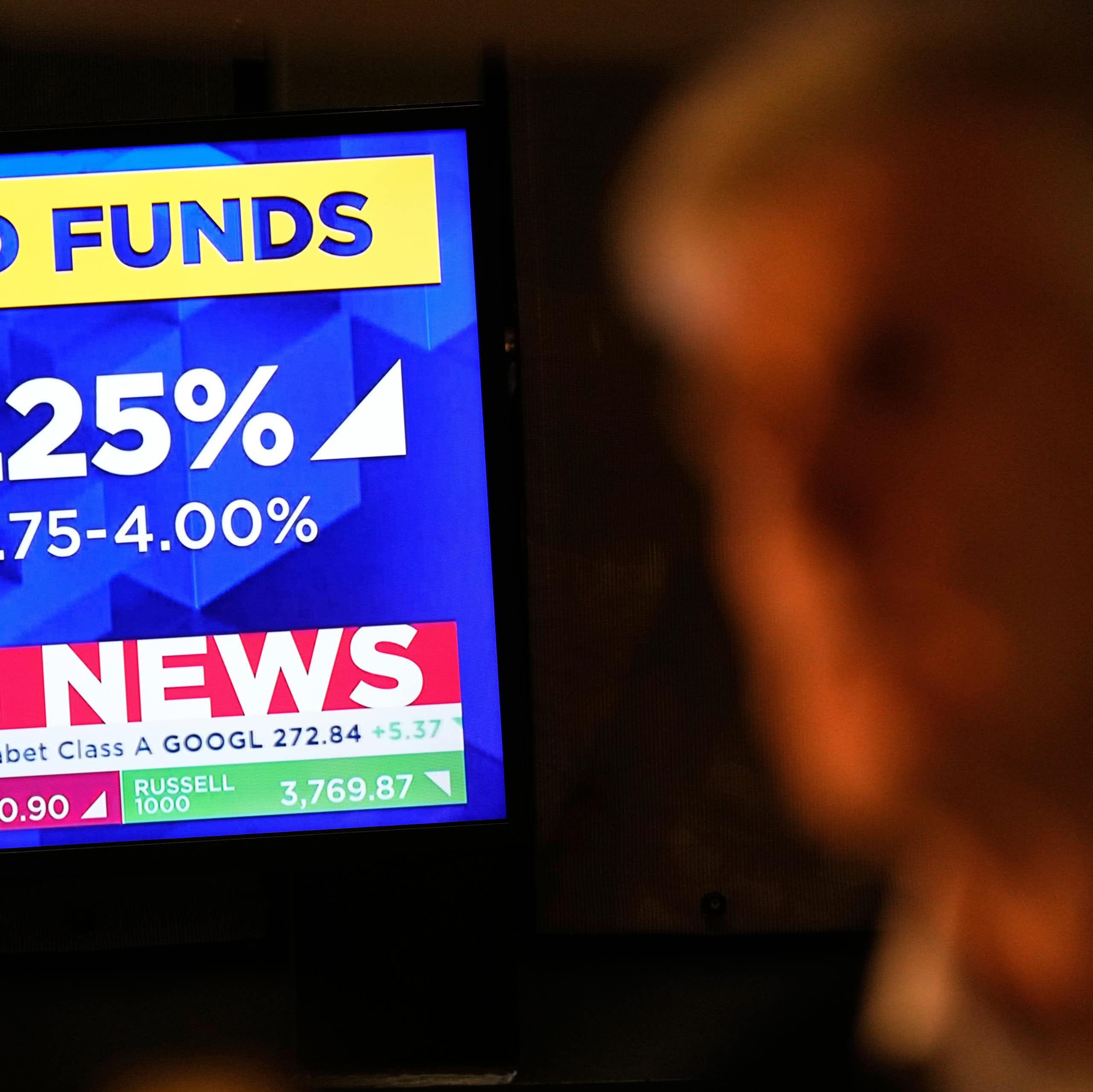 A tv screen displays news about the fed rate cut as a trader looks on
