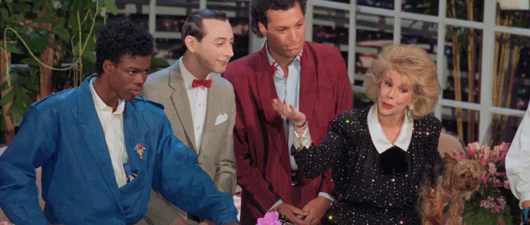 A petite woman holding a tiny dog stands next to three men on a TV set.