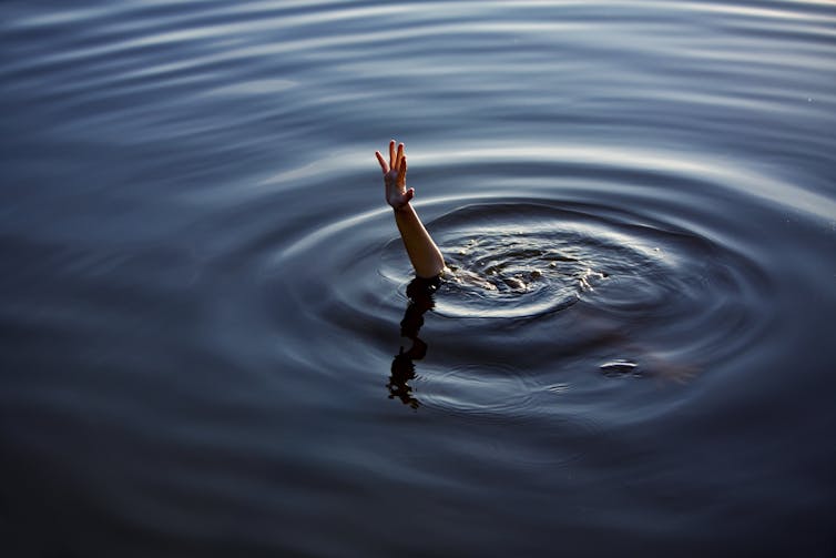 a hand reaches out of the water with circular ripples around