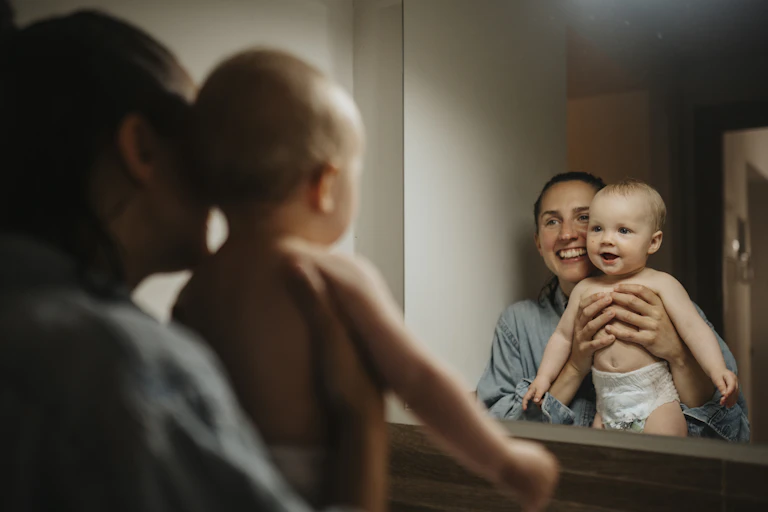 A woman holds a baby up to a mirror.