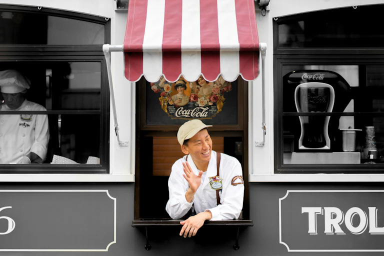 A man in uniform waves from an old school trolley at a passing customer.