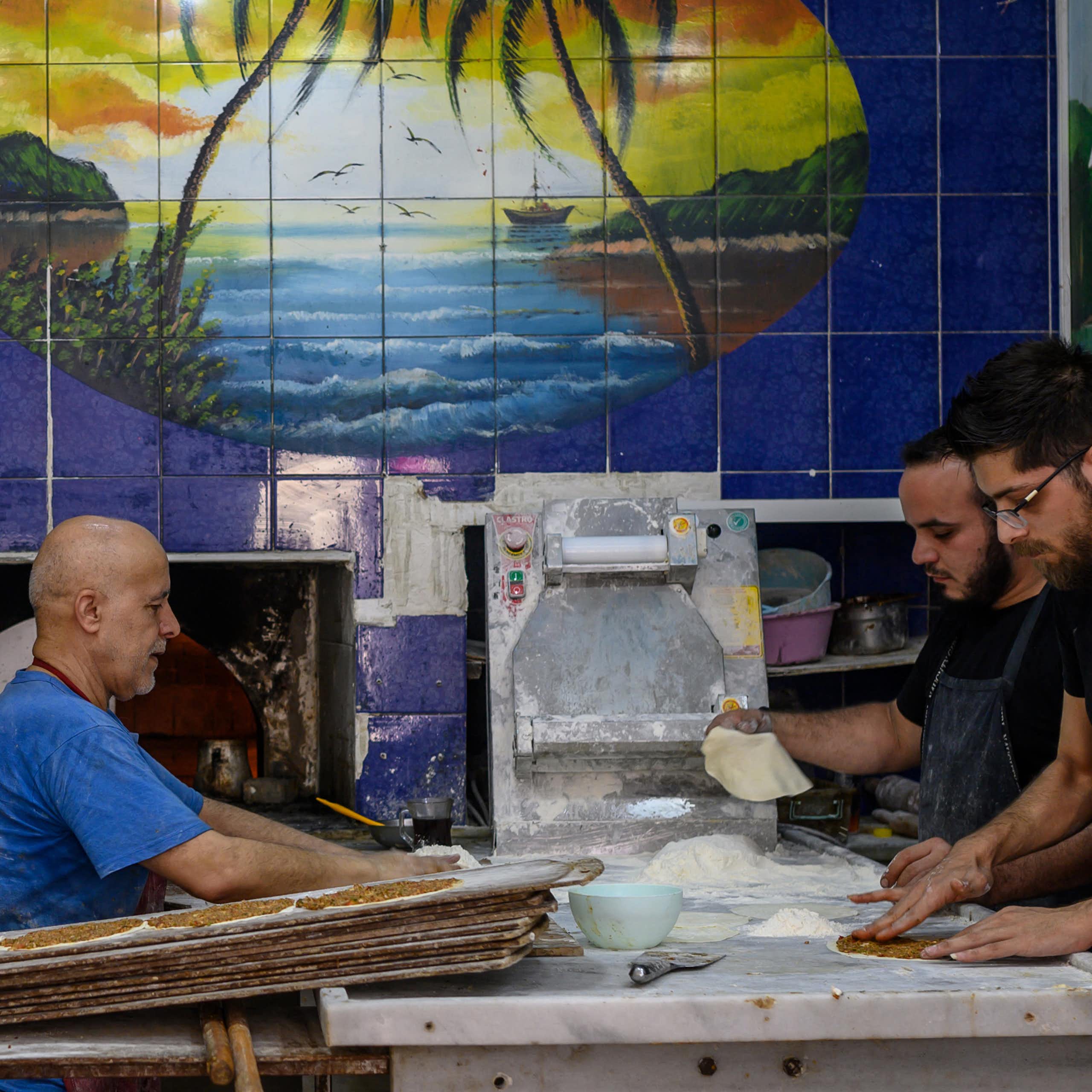 Three men work inside a bakery with blue-tiled walls.