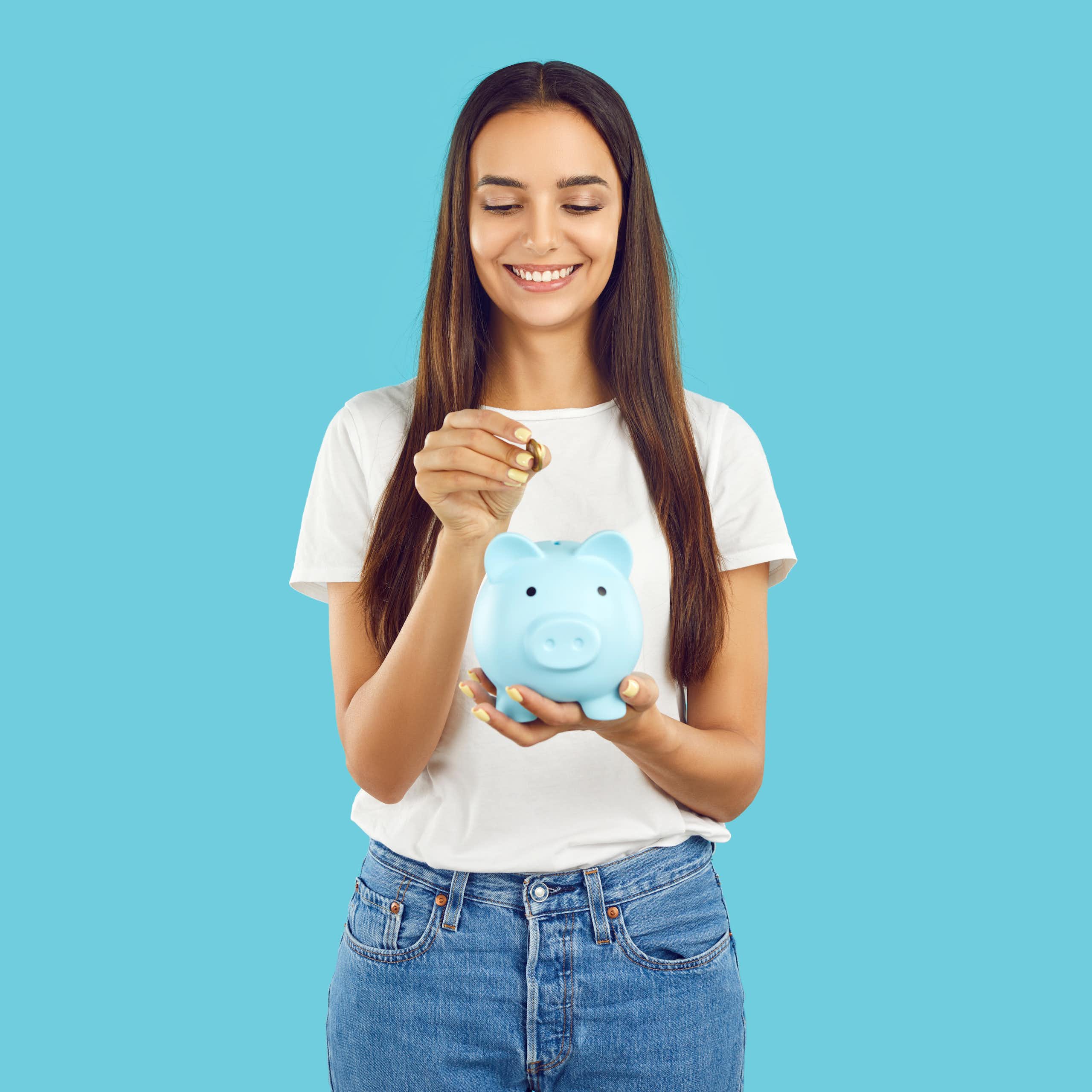 blue background, woman smiling putting coin into blue piggy bank