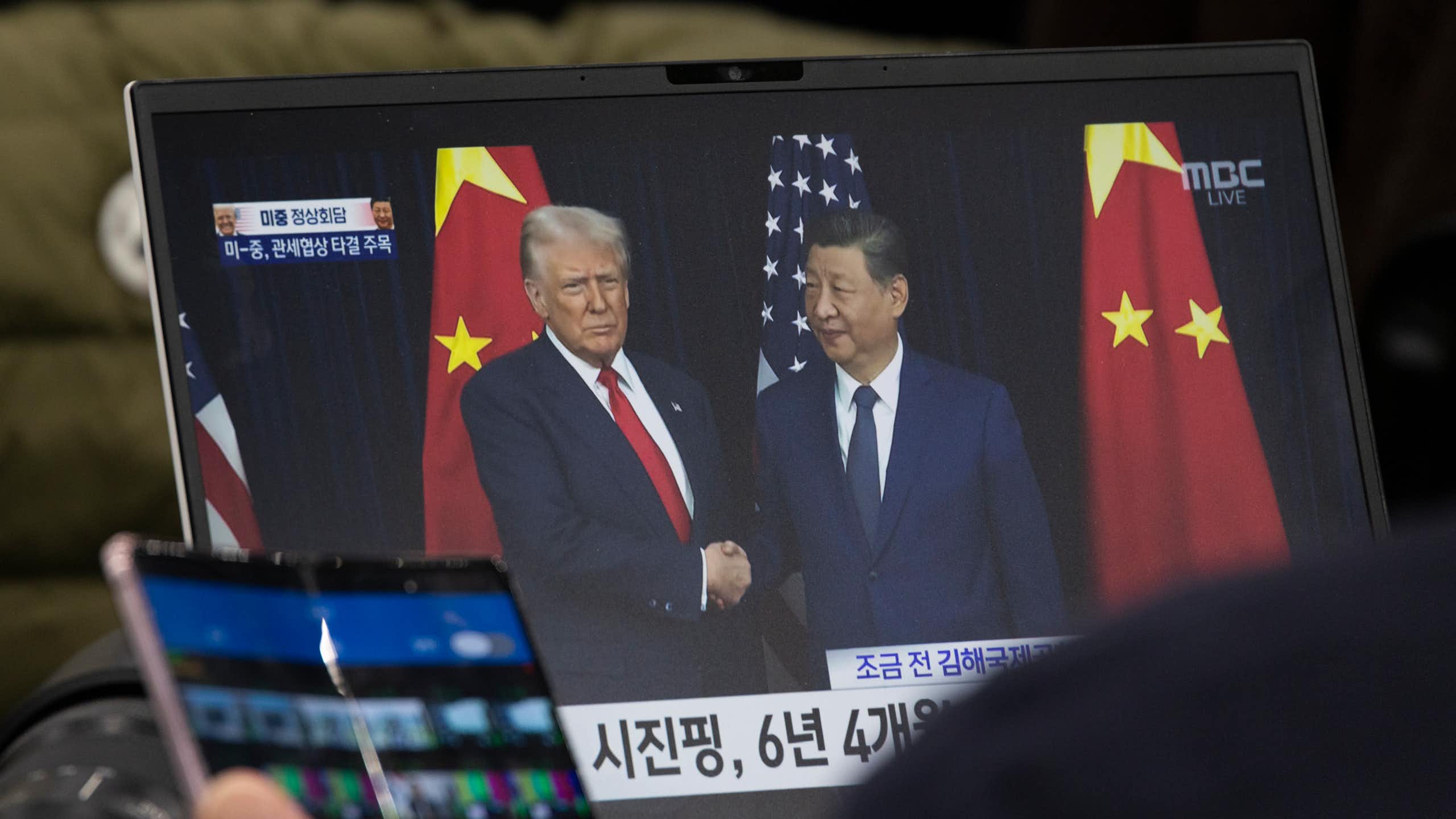 A laptop screen displaying Donald Trump and Xi Jinping shaking hands.
