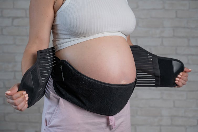 Mid-section view of a pregnant person wearing a back support strap around their belly.