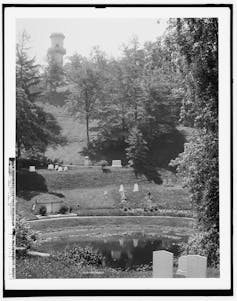A black-and-white image of a cemetery on a hill, with a tower atop the hill and trees scattered throughout.