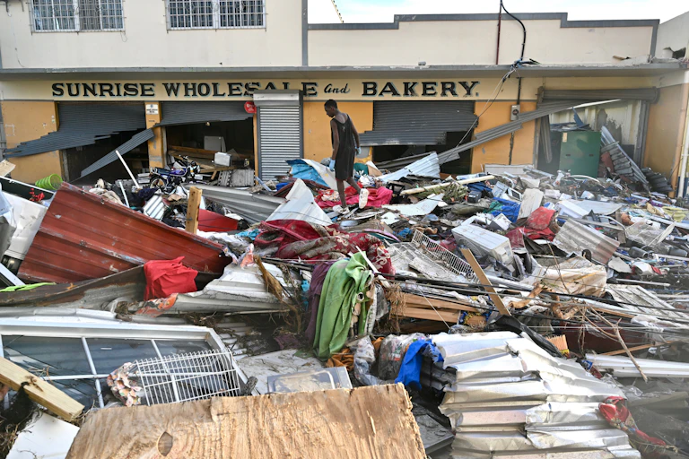 A man walks through debris from roofs and windows in front of a bakery.
