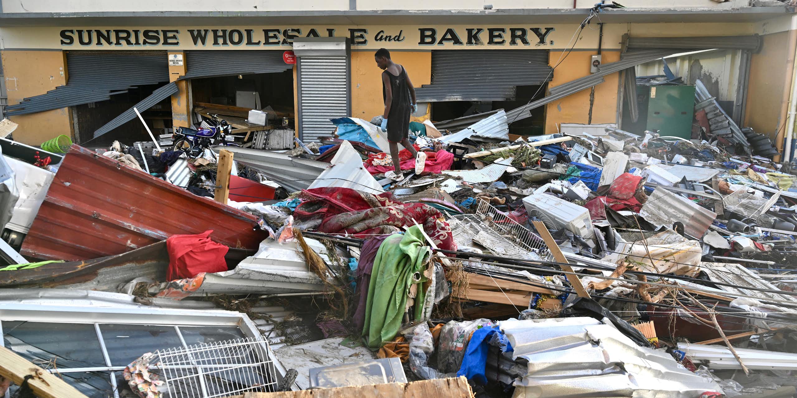 A man walks through debris from roofs and windows in front of a bakery.