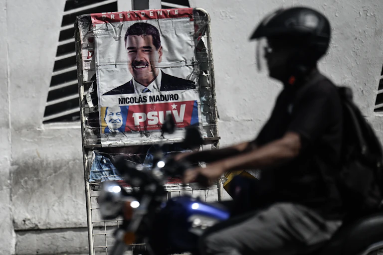 A man in a helmet and on a motorcycle drives past a poster with a a man's face.