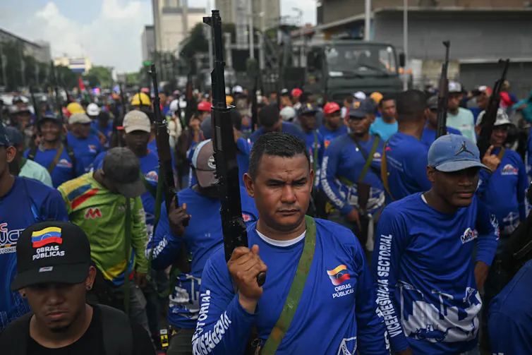 Men and women in blue tops hold guns and march.