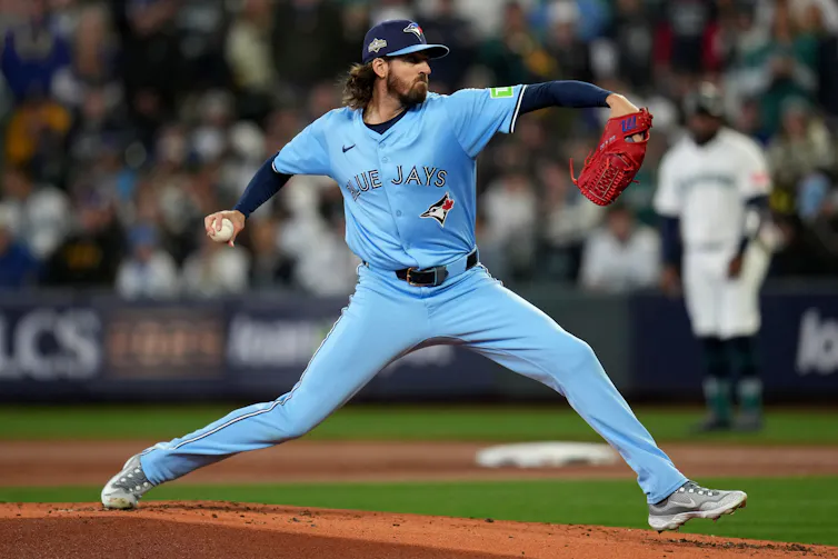 A pitcher with longish brown hair wearing a Toronto Blue Jays uniform extends himself while pitching.