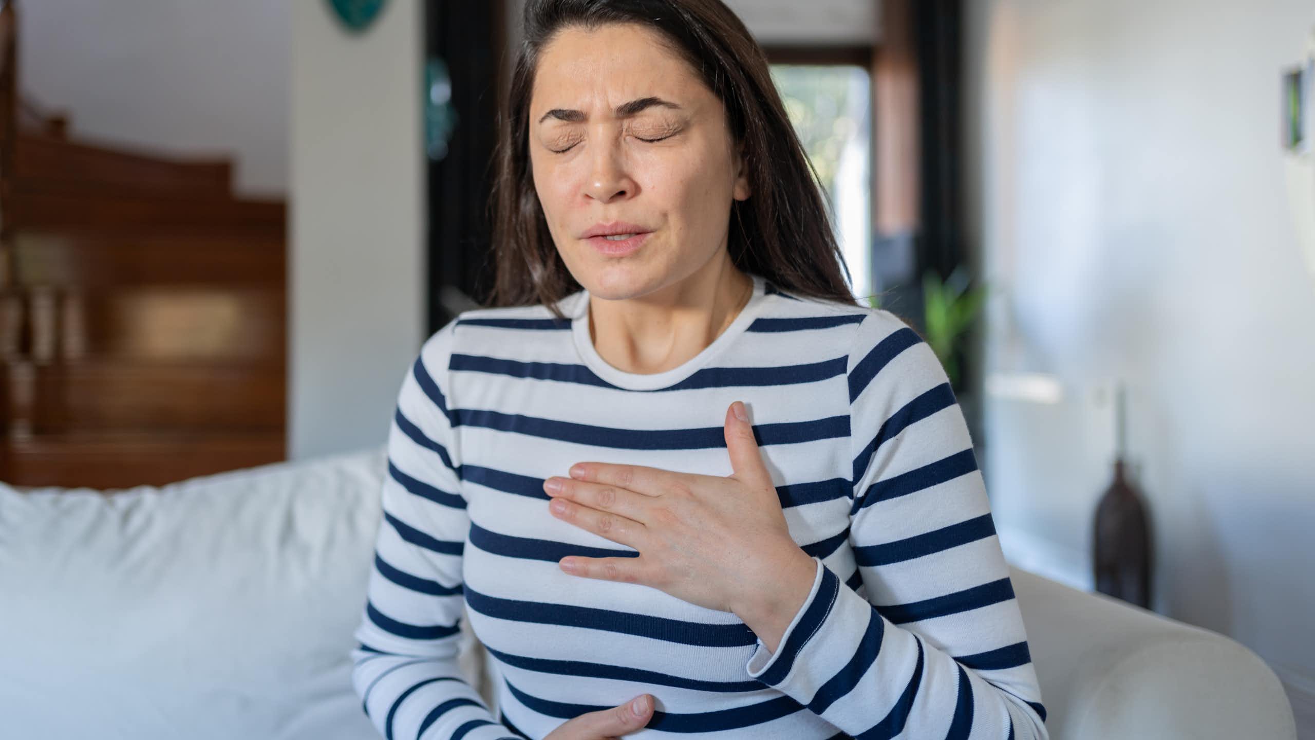 Young woman holding her hands to her chest and stomach as if in pain.