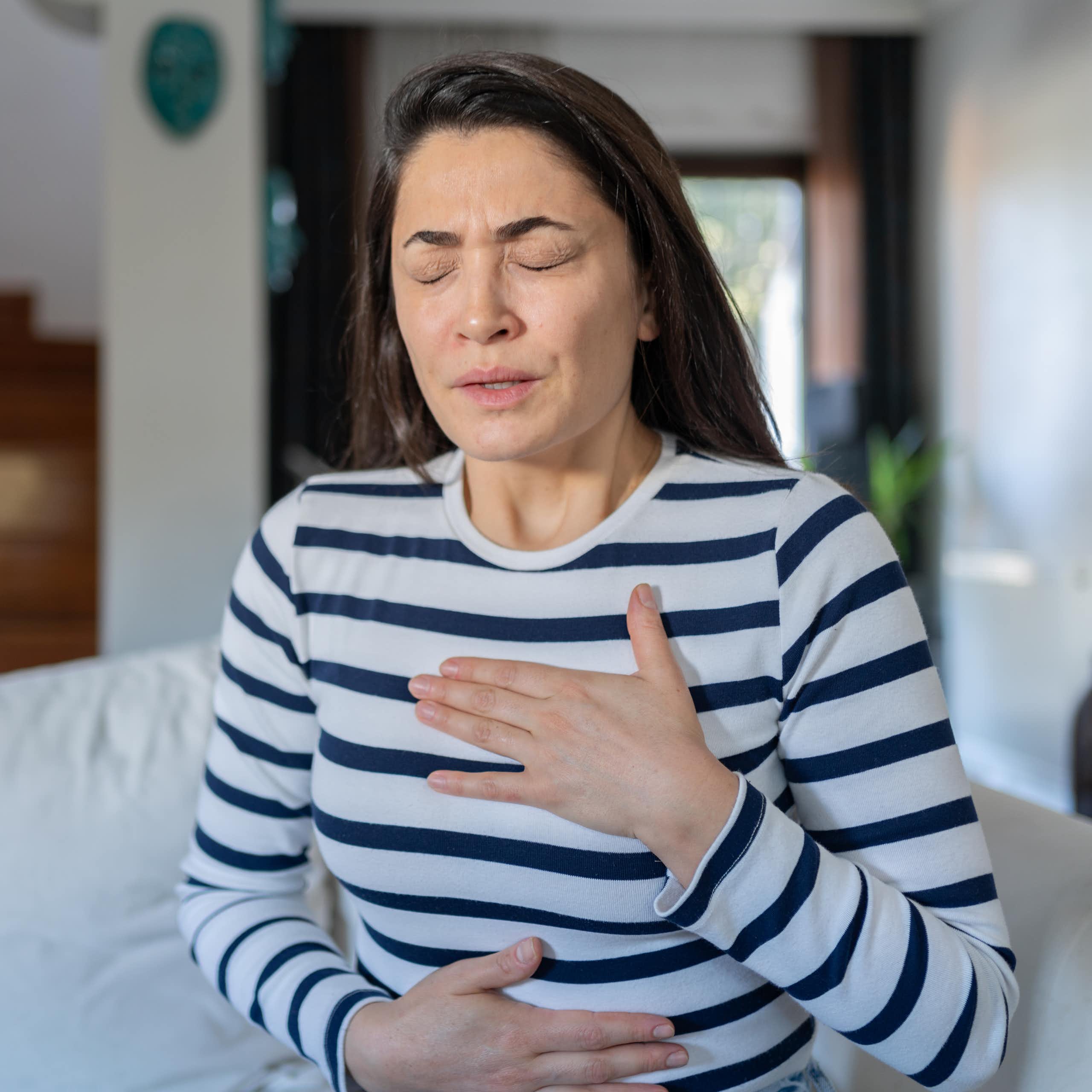Young woman holding her hands to her chest and stomach as if in pain.