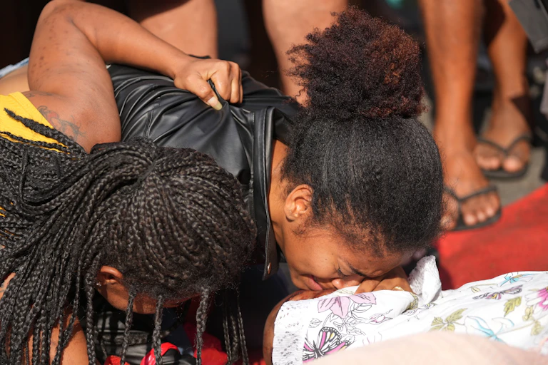 Uma jovem negra chora sobre o corpo de uma pessoa envolta em um lençol