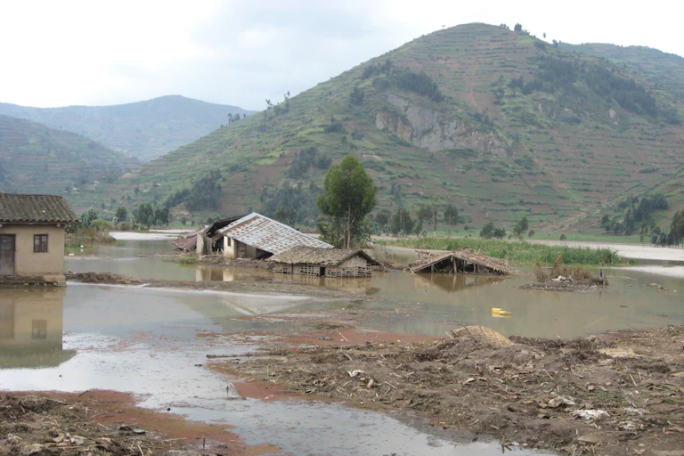 A flooded small farm with a mountain in the background, with buildings collapsing and crops covered with muddy water