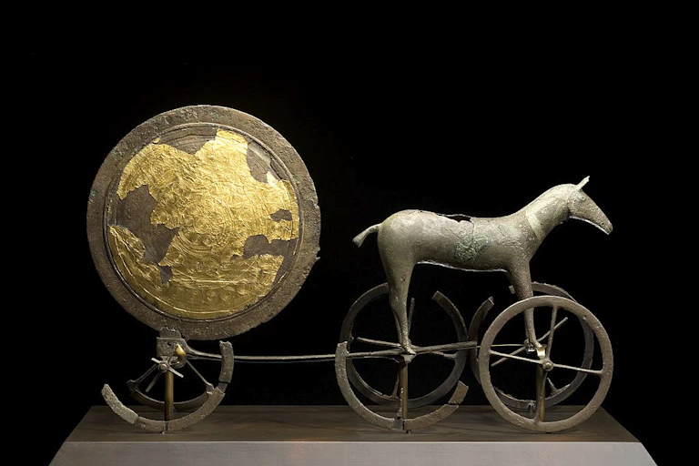 Un char en bronze et en or représentant un cheval sur des roues suivi d'un bouclier.