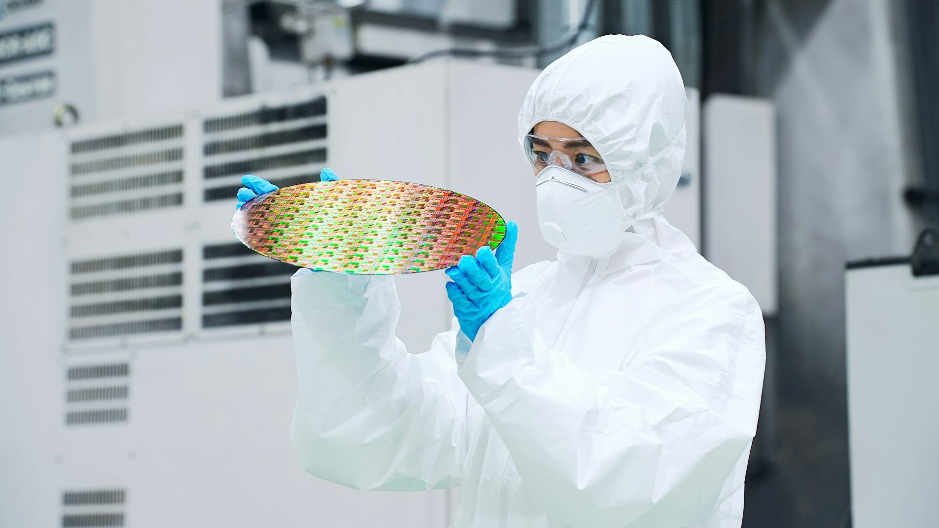 Una mujer con mono y mascarilla blancos sostiene un disco de un material reflectante y multicolor 