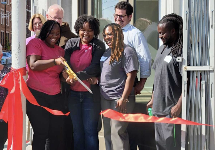 A group of people smile as two women cut a red ribbon.