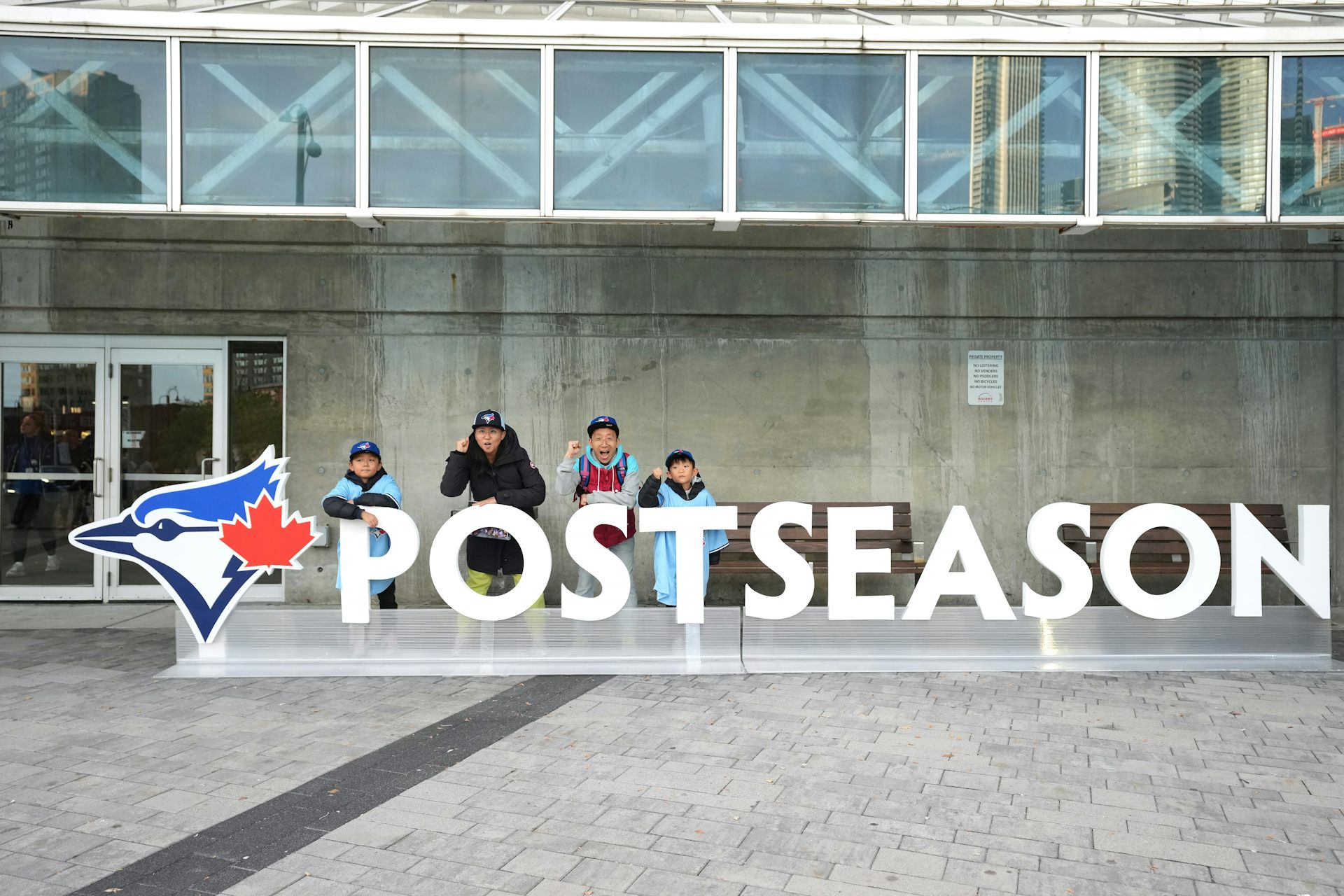People pose with a sign that says 'postseason' beside the Toronto Blue Jays logo