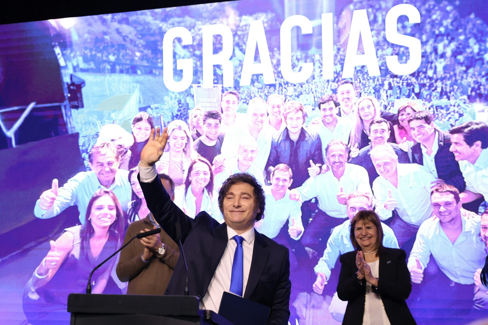 argentinian president javier milei gives a celebratory speech in front of a backdrop reading 'gracias'