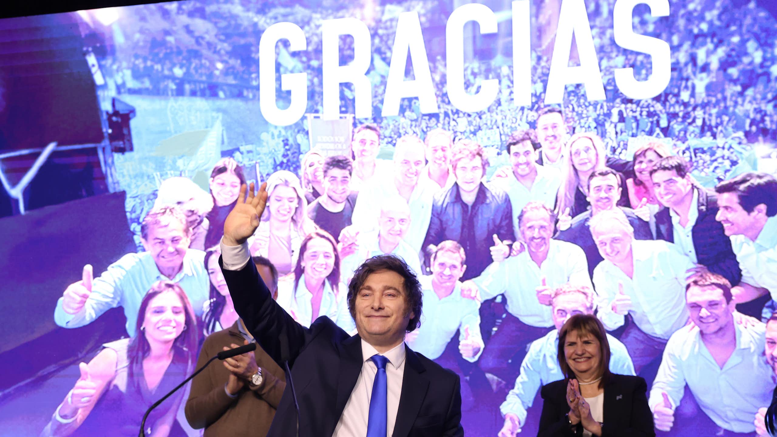 argentinian president javier milei gives a celebratory speech in front of a backdrop reading 'gracias'