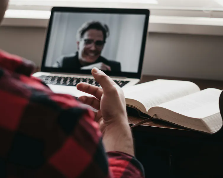A person onscreen speaks to a person sitting at a laptop.