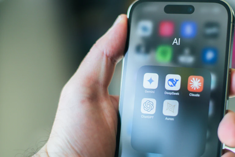 A hand holds a smartphone showing various AI apps.