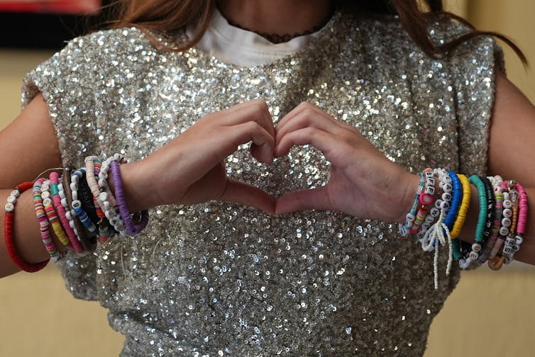 Una niña hace un símbolo de corazón con sus manos mientras usa muchas pulseras de la amistad.