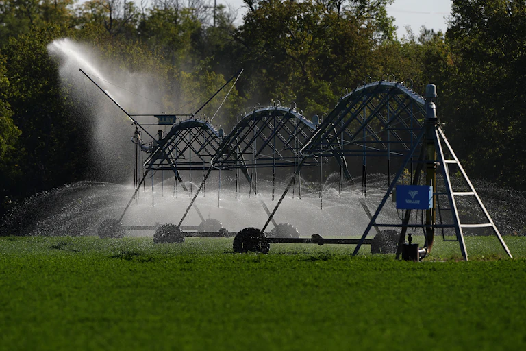 A set of metal tubes sprays water on a field.