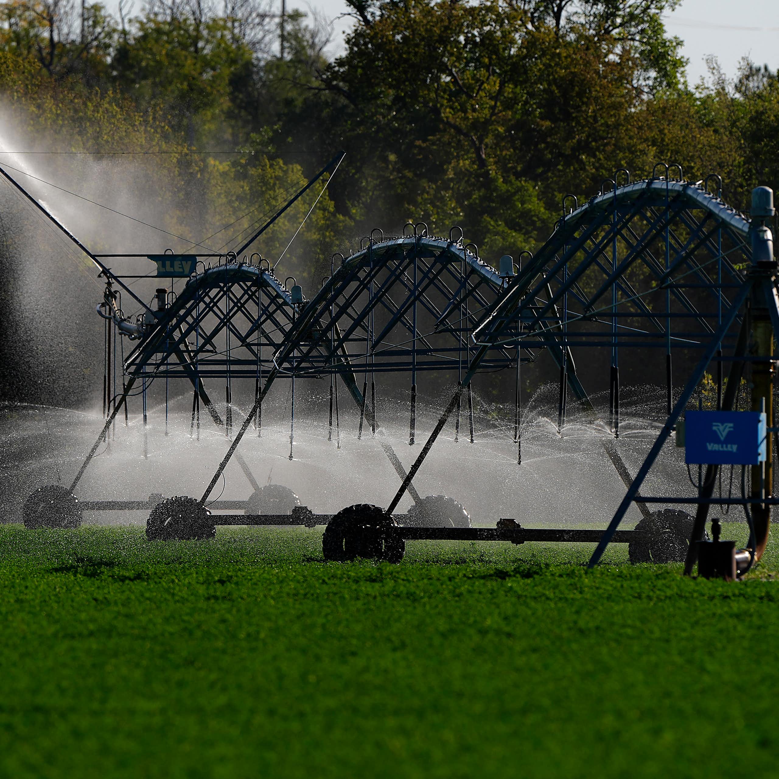 A set of metal tubes sprays water on a field.