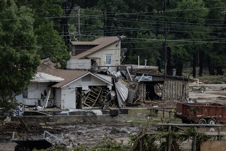 A flood-damaged house is covered in mud and debris.