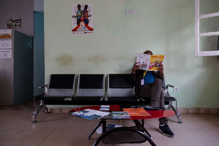 Person sitting in an empty waiting room with a magazine covering their face