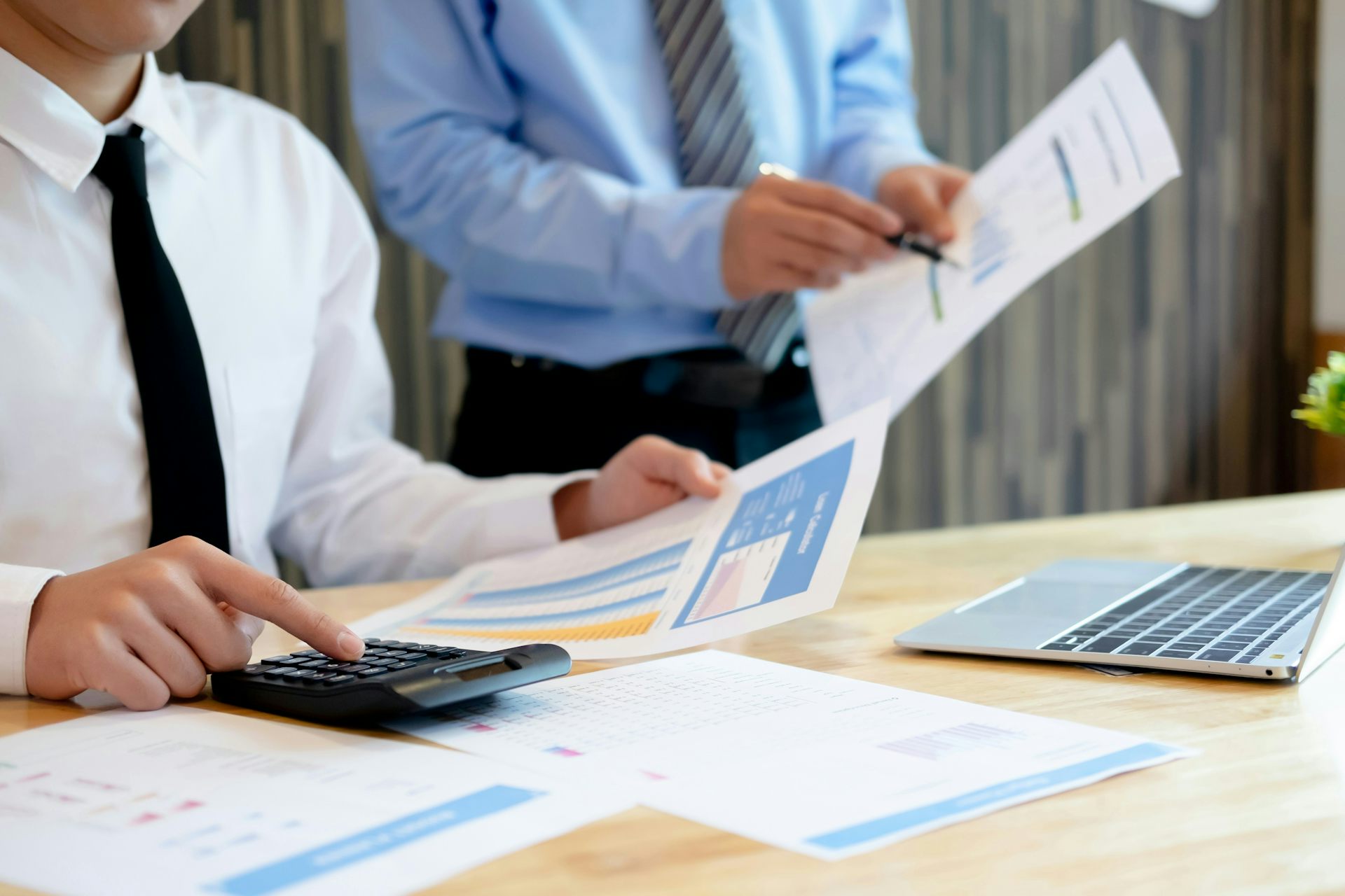 Una persona, vista desde el pecho hacia abajo, señala algo en un papel mientras se lo muestra a otra persona sentada a su lado.