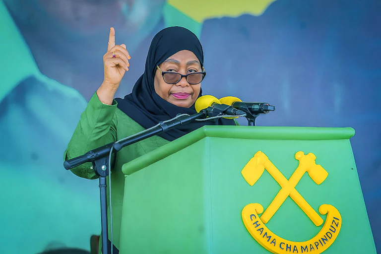 A woman dressed in green speaking into a microphone mounted on a podium written Chama Cha Mapinduzi