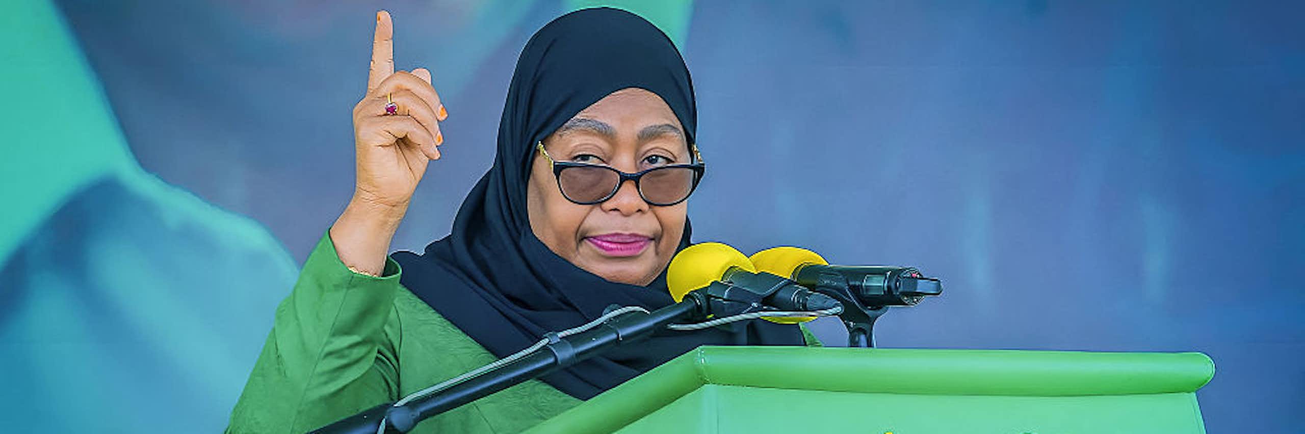 A woman dressed in green speaking into a microphone mounted on a podium written Chama Cha Mapinduzi