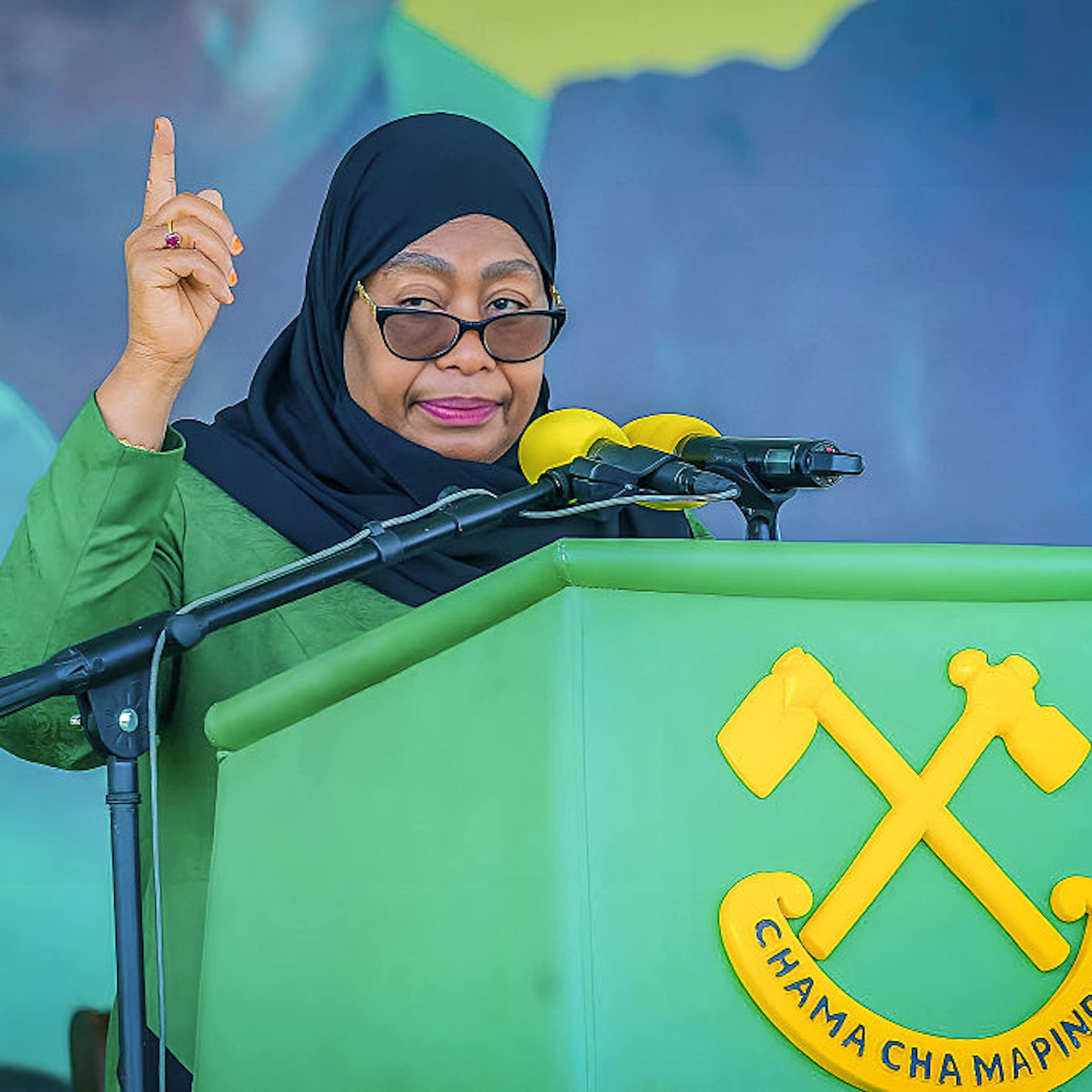 A woman dressed in green speaking into a microphone mounted on a podium written Chama Cha Mapinduzi