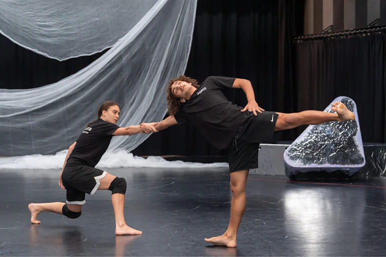 Two theatre performers, both wearing black, rehearse a dance in a studio.