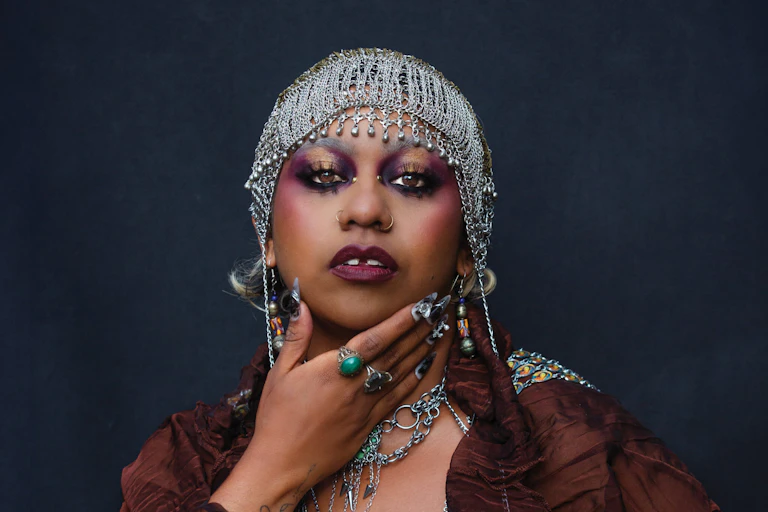 A young First Nations woman poses for the camera in bold makeup and a chainmail headdress.