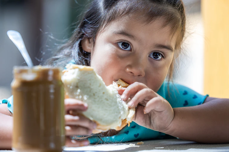 Child wearing a turquoise top eats a peanut butter sandwich